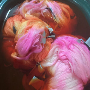 Skeins of yarn in a pot of pink dye.