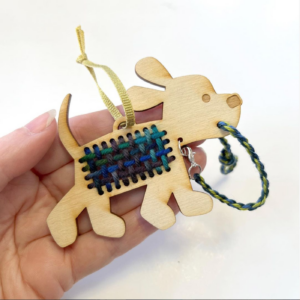 A handcrafted wooden ornament in the shape of a puppy with a small loom weave in the center, held in a hand.