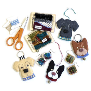 A collection of small craft kits, including tiny looms with woven designs, felt dog ornaments, and a pair of earrings, with a pair of orange scissors nearby.