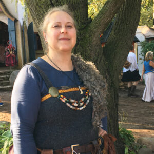 A woman at a Renaissance Faire dressed in medieval-inspired attire, standing beside a tree.