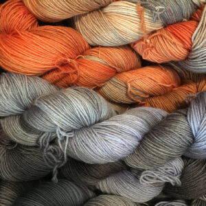 A collection of yarn skeins in varying shades of grey, orange, and brown, showcasing a natural color palette.