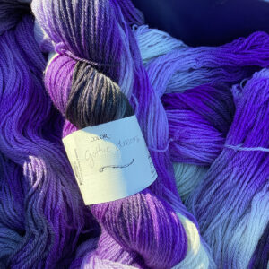 A close-up of assorted yarn skeins in shades of purple and lavender, labeled "Gothic Dreams."